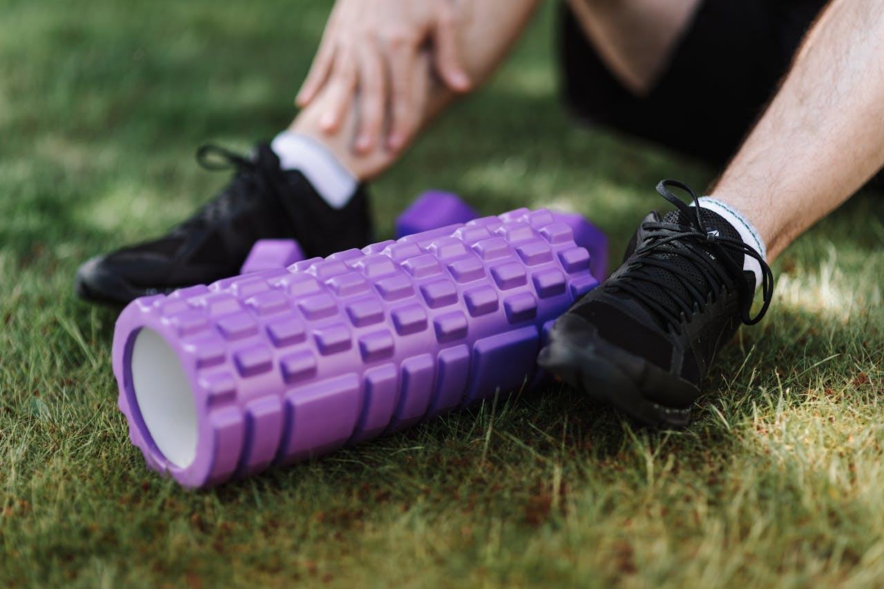 Black sneakers and purple foam roller on grass, outdoor fitness scene.